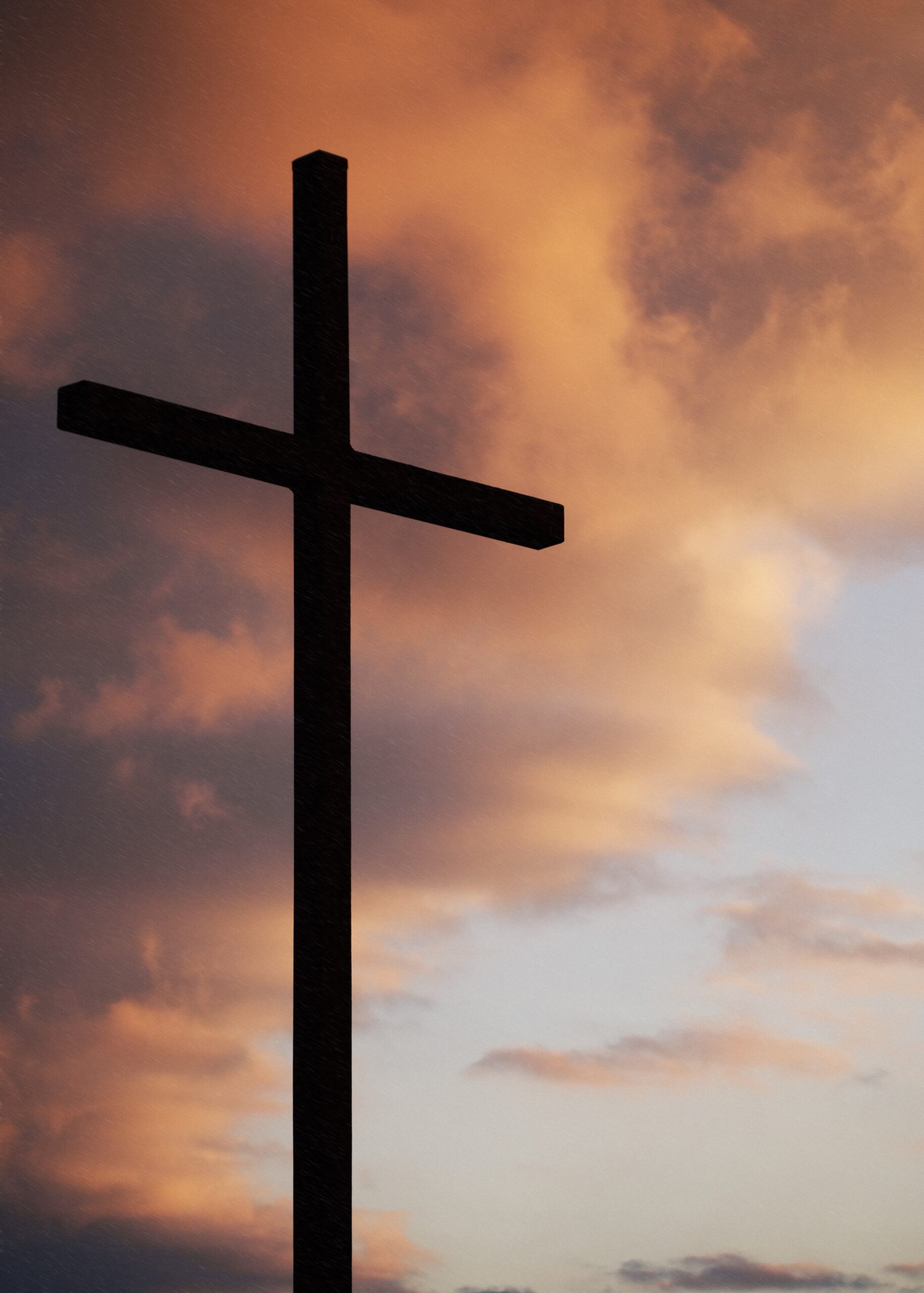 A wooden cross silhouetted against a colorful sunset sky
